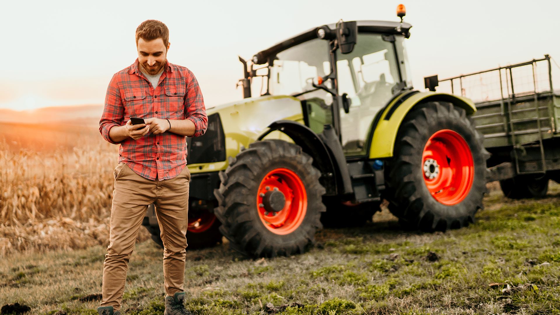 Man on his phone in front of a tractor in a wheat field